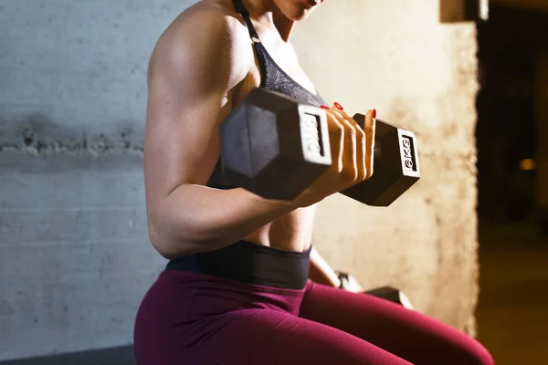 Vista de cerca de una fuerte musculatura construir fitness mujer levantamiento de peso y el entrenamiento de bíceps en el gimnasio . — Foto de Stock