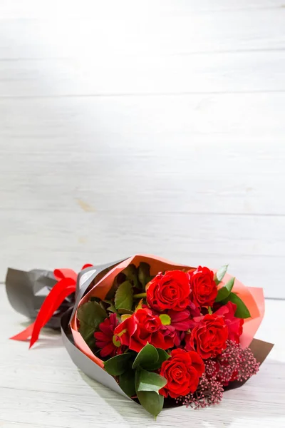 明るい木製の背景に黒い紙に赤いバラ — ストック写真