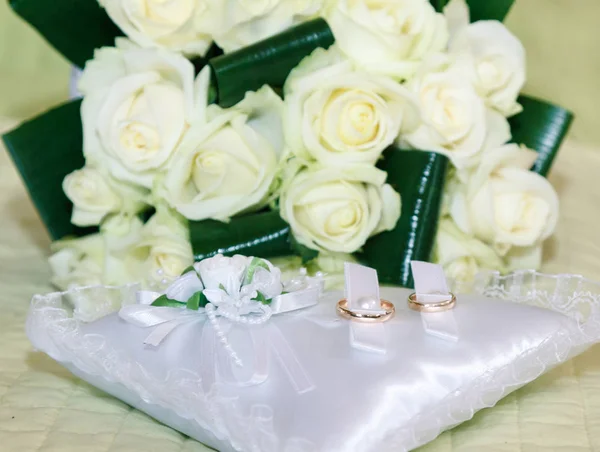 在白色缎子婚礼靠垫上的结婚戒指对一束白玫瑰 — 图库照片