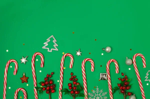 緑の背景にクリスマスの組成。キャンディ缶、赤い果実のクリスマスフレーム. — ストック写真