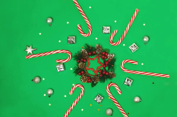 緑の背景にクリスマスの組成。キャンディ缶、赤い果実のクリスマスフレーム. — ストック写真