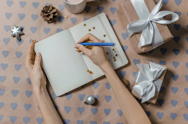 Female writing wish list in to notebook near gifts — Stock Photo, Image
