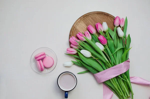 Kaffekopp, vårtulpanblommor och rosa makaroner på pastellbordet ovanifrån. Hälsning för kvinnor eller mödrar dag — Stockfoto