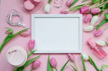 White picture with coffee cup, spring tulip flowers and pink macarons on pastel table top view. Greeting for Mothers Day
