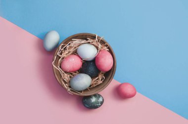 Easter greeting background with dyed multicolored chicken quail eggs on straw in plate