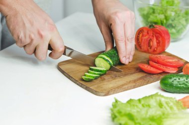 Erkek eller salata hazırlıyor. Salatalık kesmek. Sağlıklı yemek kavramı.