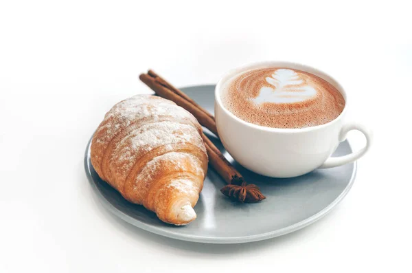 Kahve fincanı, latte sanatı ve tarçınlı taze kruvasan.