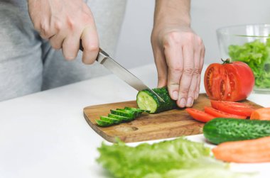Erkek eller salata hazırlıyor. Salatalık kesmek. Sağlıklı yemek kavramı.