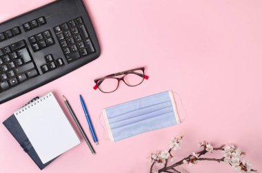 Tıbbi maskeli, klavyeli, pembe arka planda not defteri olan çiçek açan dallar. Coronavirus COVID-19