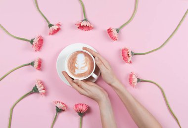 Kahve fincanı ve pembe çiçekli latte tabağı tutan eller.