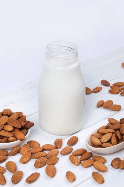 Şişede badem sütü ve beyaz ahşap arka planda badem fıstığı