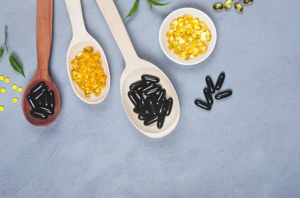 Black and yellow pills on wooden spoon on gray background — Stock Photo, Image