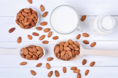 Bardakta badem sütü, tohumlar ve tahta kaşıklar beyaz tahta tabakta.