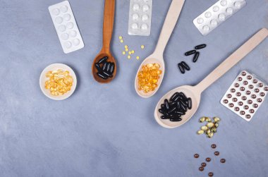 Tahta kaşıklarda siyah ve sarı haplar ya da gri arka planda paketlenmiş