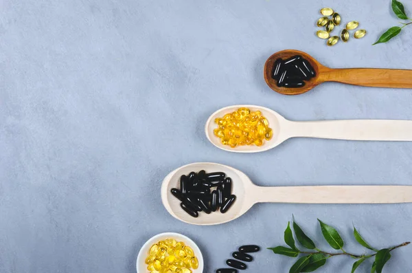 Black Pills Yellow Pill Wooden Spoons Grey Background — Stock Photo, Image