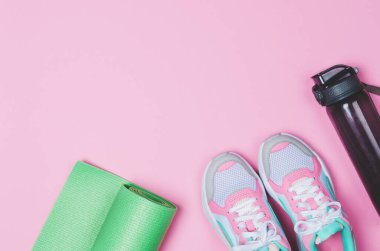 Yoga minderi, spor ayakkabılar, pembe arka planda bir şişe su. Sağlıklı bir yaşam tarzı. Boşluğu kopyala