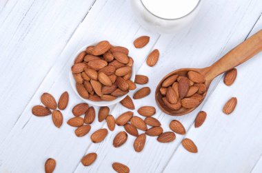 Badem sütü, badem tohumları ve tahta kaşıkla beyaz ahşap masa.