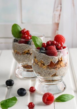Chia puding taze çilek, ahududu ve yaban mersini ile iki kadeh. Çilek sepetle. Ahşap hafif bir arka plan üzerinde.