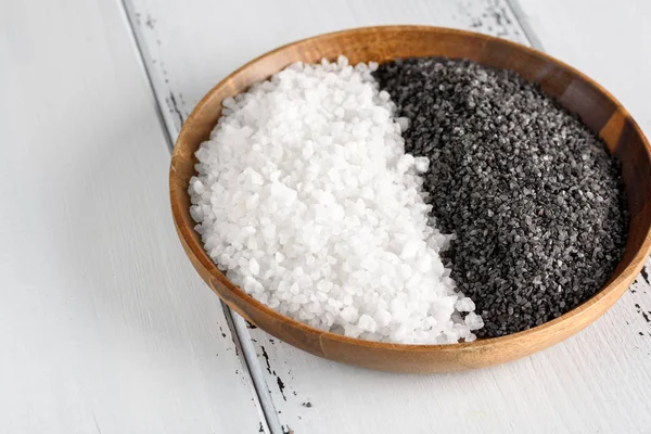 Два вида соли. Белая морская соль и черная гималайская соль в деревянной чаше на белом фоне — стоковое фото