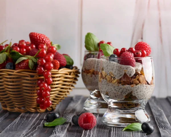 Chia puding taze çilek, ahududu ve yaban mersini ile iki kadeh. Çilek sepetle. Ahşap bir gri arka plan üzerinde. — Stok fotoğraf