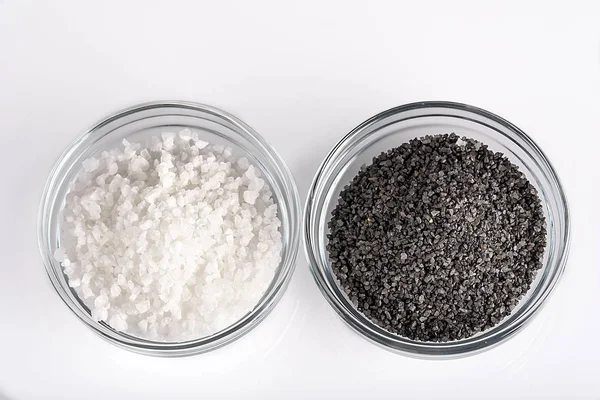 Dos tipos de sal. Sal marina blanca y sal negra del Himalaya en un recipiente de vidrio aislado sobre fondo blanco — Foto de Stock