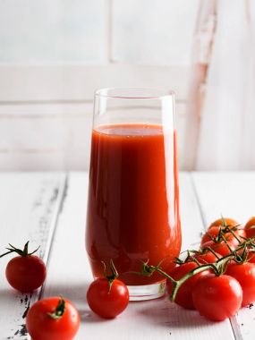 Bir kiraz ve fesleğen üzerinde hafif bir arka plan ile bir bardak domates suyu