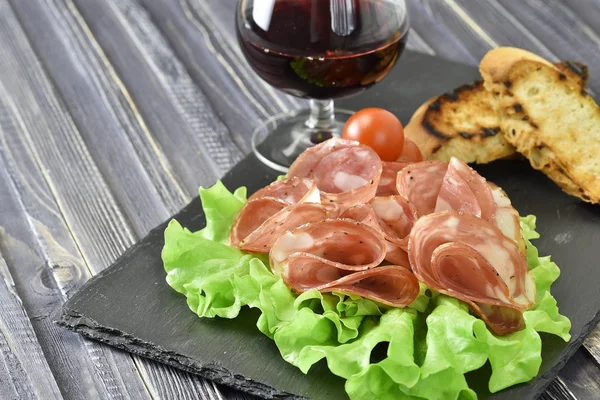 Cold meat plate. Sliced ham with lettuce leaves on a dark stone background, selective focus — Stock Photo, Image