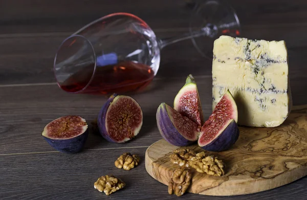Cheese roquefort with figs, nuts and a glass of red wine on a wo