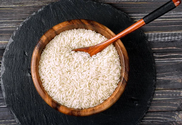 Isolated handfull of raw rice in the wood bowl on black stone bac