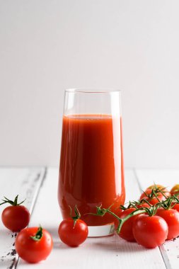 Bir kiraz ve fesleğen üzerinde hafif bir backg ile bir bardak domates suyu