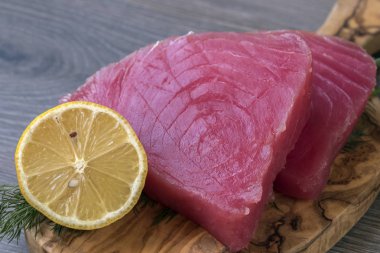 Dereotu, limon ve zeytin kesme tahtası içinde biber ile ham ton balığı filetosu
