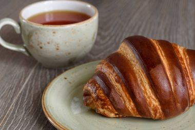 Taze kruvasanlar ve ahşap vintage sekmesinde kahvaltıda çay bardağı