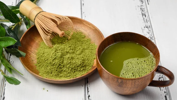 Green tea matcha powder in a wooden bowl with a whisk