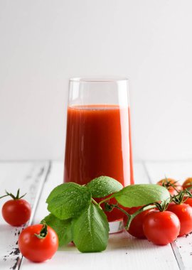 Bir kiraz ve fesleğen üzerinde hafif bir backg ile bir bardak domates suyu