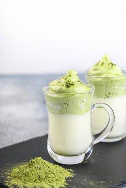 İki fincan Dalgona Matcha Latte, kremalı çırpılmış kibrit, açık arkaplanda. Kibrit yeşil çay.