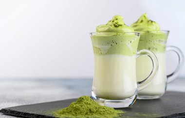 İki fincan Dalgona Matcha Latte, kremalı çırpılmış kibrit, açık arkaplanda. Kibrit yeşil çay.
