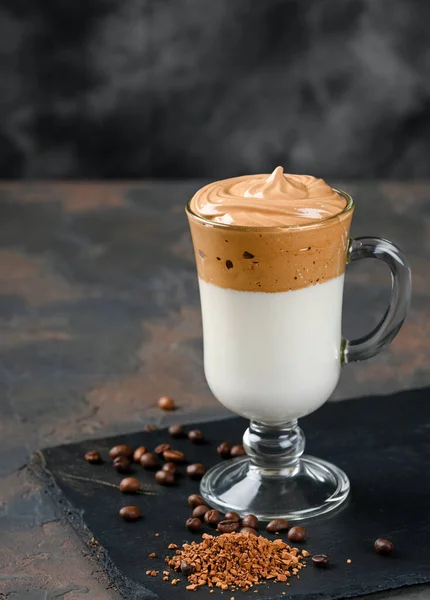 Glass cup with Dalgona frothy coffee trend korean drink latte espresso with coffee foam on black background.
