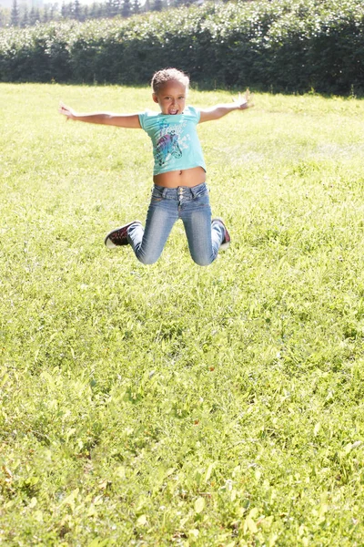 Little girl. Bounce. Juicy green grass — Stock Photo, Image