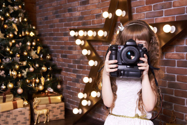 A girl with a camera. A small photographer. Christmas interior