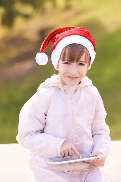 Κορίτσι με ένα δισκίο. Χαμογελαστό παιδί. Χριστουγεννιάτικο καπέλο — Φωτογραφία Αρχείου