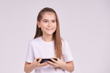 Genç ve güzel bir kız. Akıllı telefonla gülümseyen bir stüdyo resmi. Dişi ergen, arkadaşına mesaj yazıyor. Mutlu tatlı bayan çocuk.