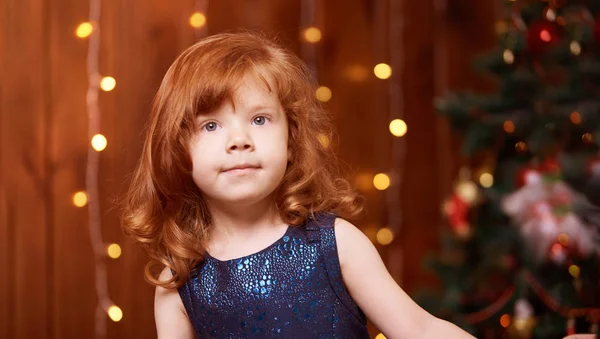 Χαρούμενο Χριστουγεννιάτικο κορίτσι. Πολυτέλεια ελκυστική κόκκινα μαλλιά παιδί. Χριστουγεννιάτικο θαύμα. Πράσινο δέντρο, φώτα, bokeh — Φωτογραφία Αρχείου