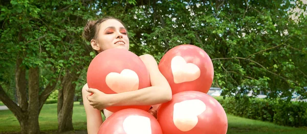 Mujer joven y bonita con maquillaje brillante. Retrato verde al aire libre. Globos rojos — Foto de Stock