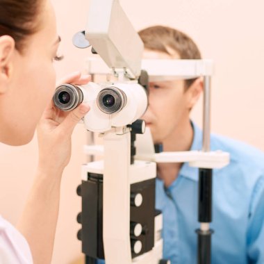 Optisyen doktor, erkek hastayla birlikte muayene laboratuvarında. Erkek gözü