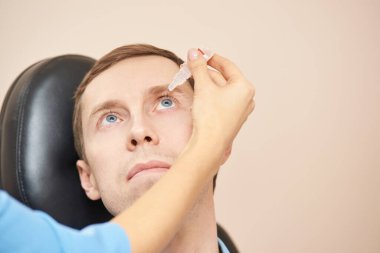 Doktor hasta yüzünün yanında göz damlası tut.