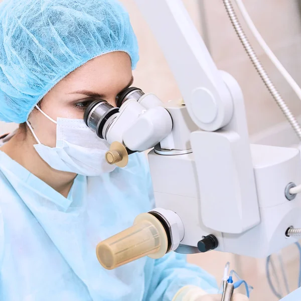 Médica na sala de operação perto do microscópio — Fotografia de Stock