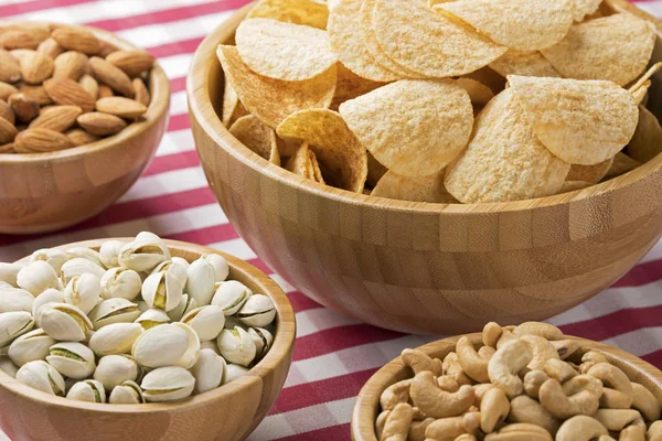 Kommen van aardappels, chips, amandelen, pistachenoten, cashewnoten op rode cheque — Stockfoto