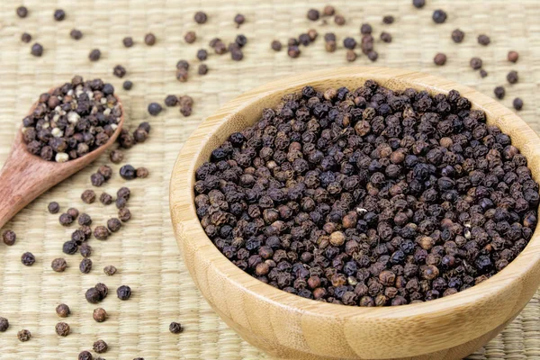 Bowl full of black peppercorns on a bamboo background
