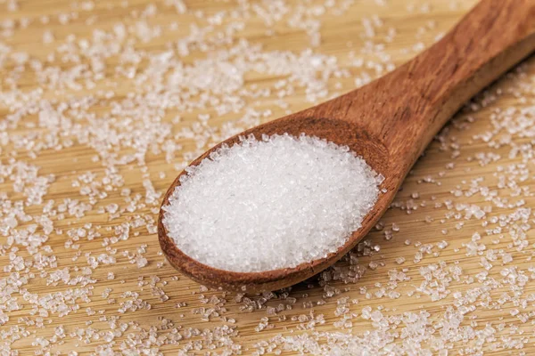 Spoon full of granulated sugar  on a wooden background