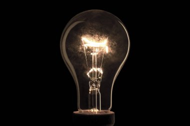Realistic light bulb on the black background. Lamp light in the dark. Electric bulb. Glowing light in the dark. clipart